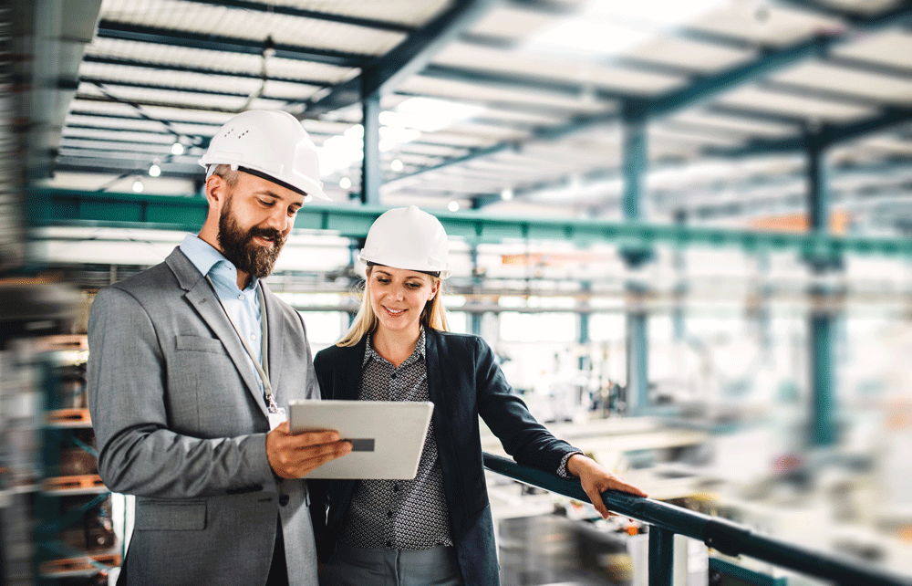 Zwei Mitarbeitende stehen in einer Fabrikhalle und bedienen ein Tablet